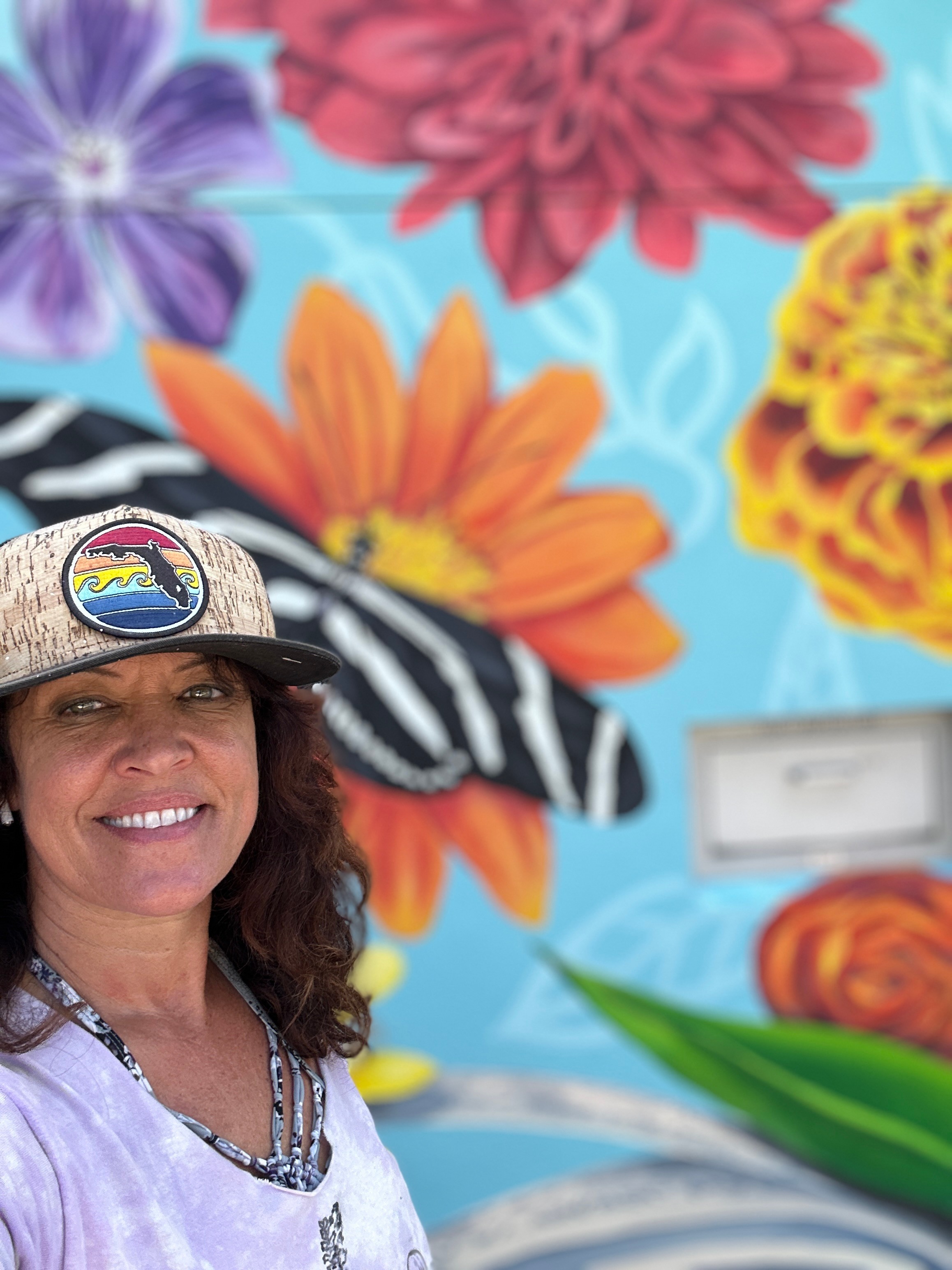 Mural artist Beth Warmath standing in front of one of her colorful floral and wildlife murals